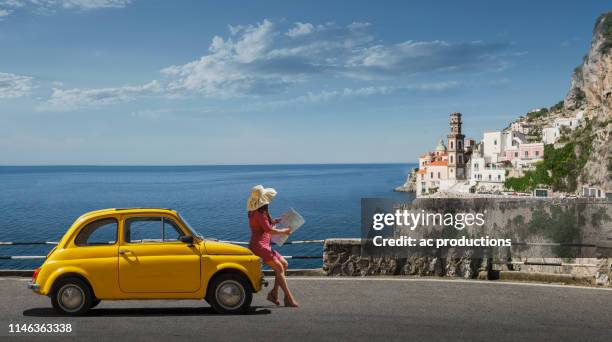 woman holding map leaning on yellow car in atrani, italy - yellow dress stock-fotos und bilder