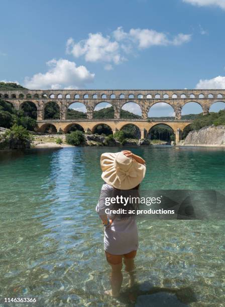 woman wearing hat standing in gardon river by pont du gard in vers-pont-du-gard, france - pont du gard aqueduct stock-fotos und bilder