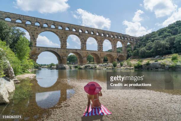 woman wearing pink hat sunbathing by pont du gard in vers-pont-du-gard, france - pont du gard aqueduct stock pictures, royalty-free photos & images