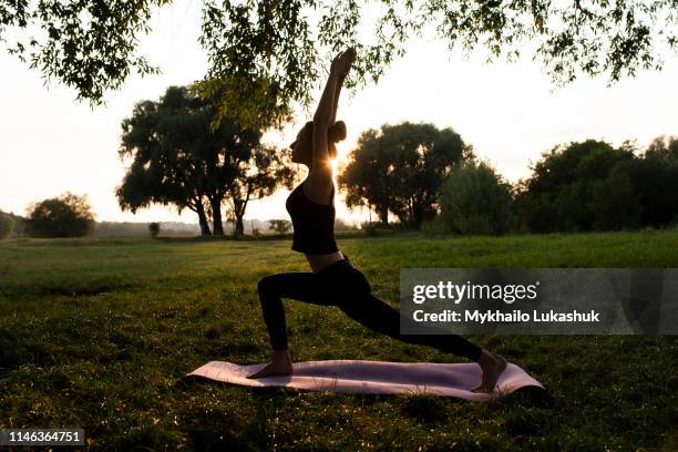 young woman practicing yoga in park at sunset - lunge silhouette stock pictures, royalty-free photos & images