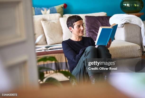 woman reading book sitting on the floor at home - literature fotografías e imágenes de stock