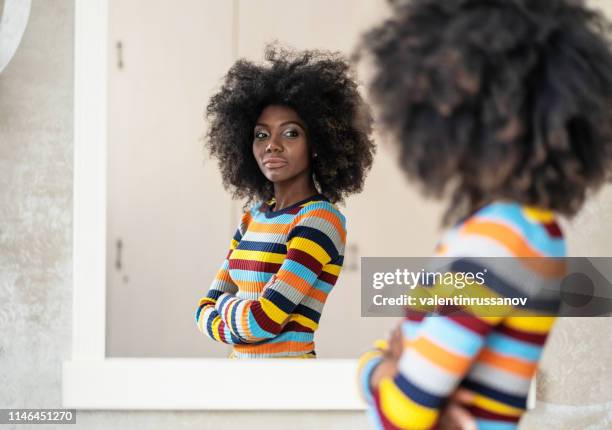 afro woman looking at her reflection in the mirror - woman mirror stock pictures, royalty-free photos & images