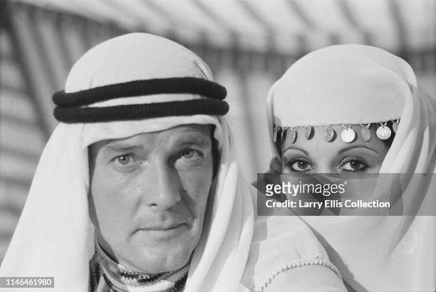 English film actor Roger Moore pictured wearing a keffiyeh in his role as James Bond with actress Dawn Rodrigues during production of the film 'The...