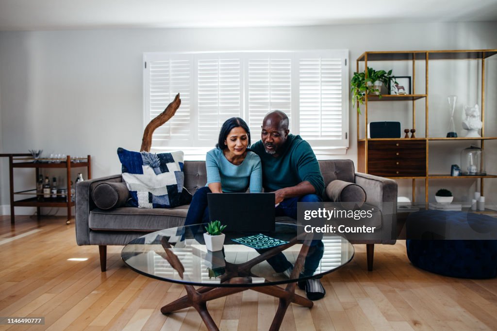 Mature married couple at home on the sofa looking at laptop