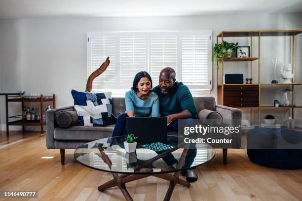 mature married couple at home on the sofa looking at laptop - retirement decisions stock pictures, royalty-free photos & images