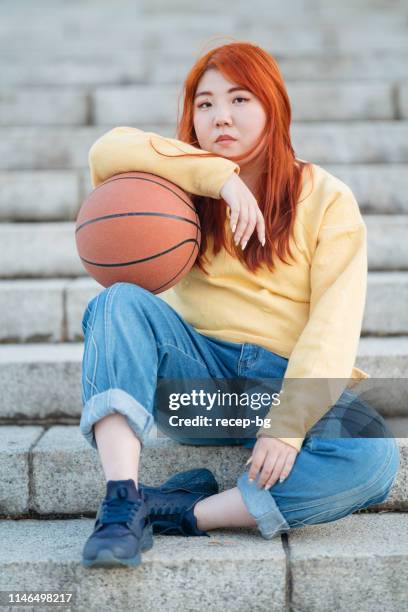 portrait of young woman holding basketball and sitting at stairs - woman yellow basketball stock pictures, royalty-free photos & images