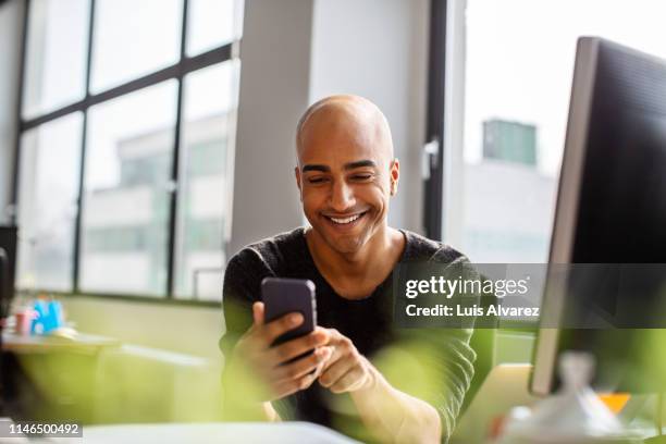 smiling mid adult man using phone at his desk - 完全に禿げている頭 ストックフォトと画像