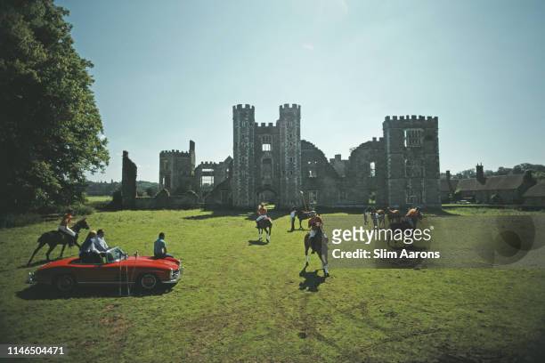 Three people sitting on a red Mercedes convertible watch polo players in action at Cowdray Park, West Sussex, August 1985. In the background are the...