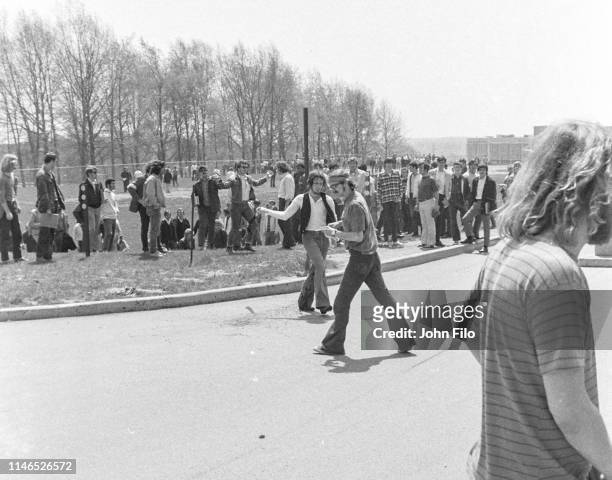 Two unidentified Kent State University students, one with a black flag, as they walk near Jeffrey Miller's blood on the pavement after the Ohio...