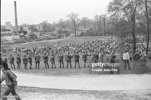 View, from behind, of a line of armed Ohio National Guardsmen as they stand at the top of Blanket Hill, facing the Commons which is full of students,...