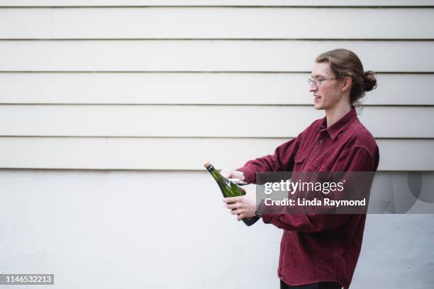 young man opening a champagne bottle - champagner korken stock-fotos und bilder