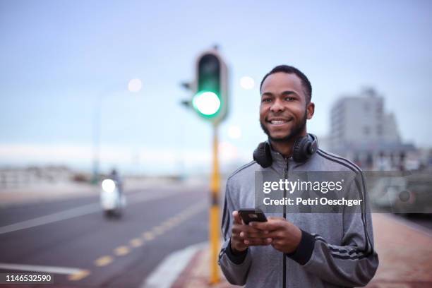 un homme africain utilisant son téléphone portable à côté d’une route publique. - man wearing cap photos et images de collection