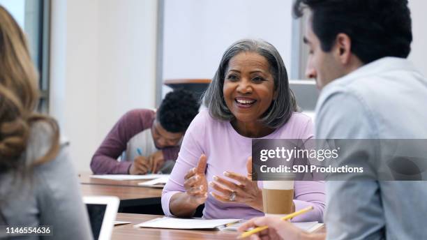 mature woman gestures while talking with classmates - principal stock pictures, royalty-free photos & images