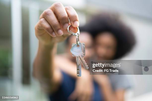 jeunes couples devant une maison, tenant les clefs de leur nouvelle maison - clé de maison photos et images de collection