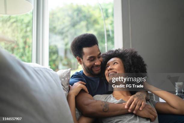 african couple lying down and having romantic moment on couch - young couple hugging stock pictures, royalty-free photos & images