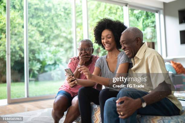 nipote afro che mostra foto nel suo cellulare ai nonni, persone che sorridono e si divertono - african american grandparents foto e immagini stock