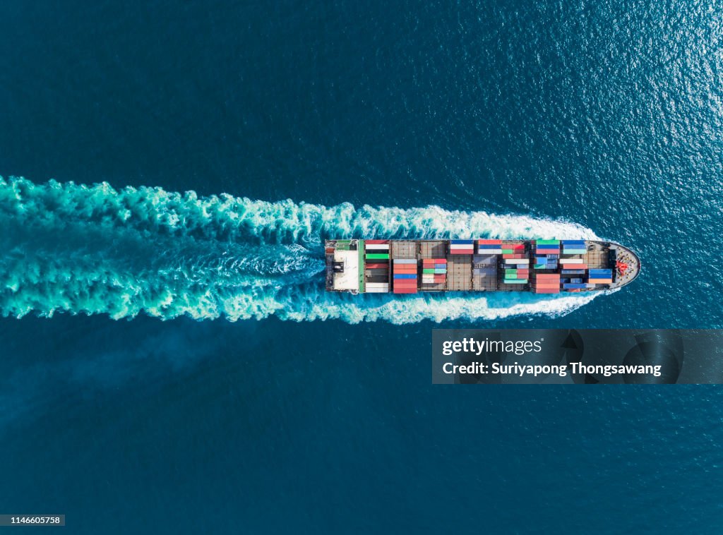 Aerial top view container ship full speed with beautiful wave pattern for logistics, import export, shipping or transportation.