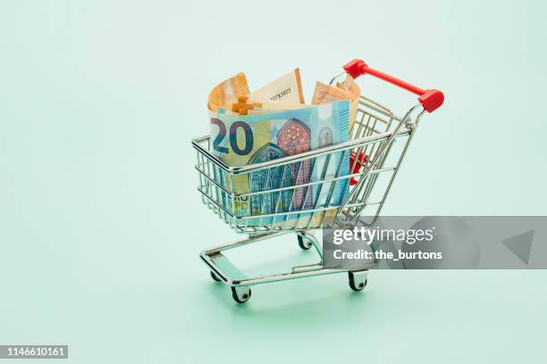still life of shopping cart and euro notes on turquoise background - paying supermarket stock-fotos und bilder