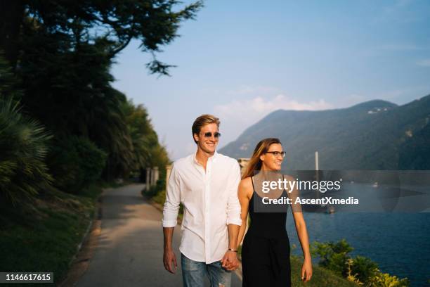 couple walk along promenade at sunset - woman look straight black shirt stock pictures, royalty-free photos & images