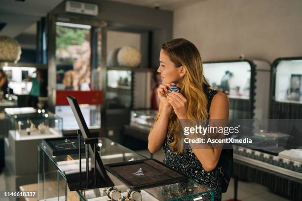 young woman smiles while trying on jewellery - jeweller stock pictures, royalty-free photos & images