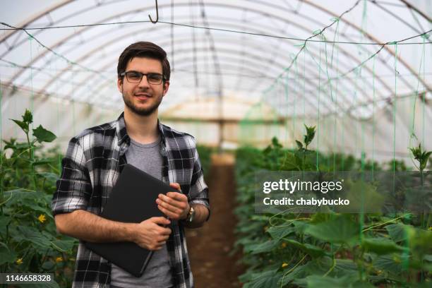 junger bauer mit laptop schaut auf kamera - agronom stock-fotos und bilder