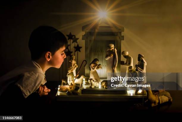 young boy leaning in looking closely at a ceramic nativity scene. - weihnachtskrippe stock-fotos und bilder