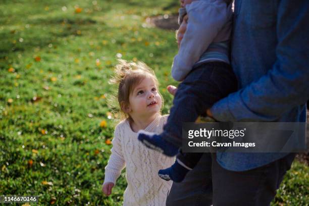 a little girl looks up at her baby brother held in her father's arms - chubby girl stock-fotos und bilder
