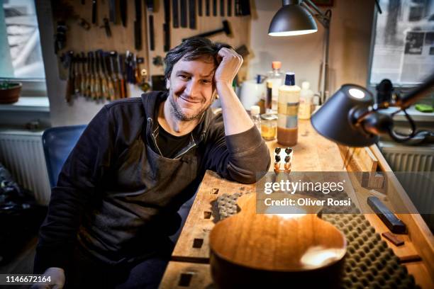 portrait of smiling instrument maker sitting in his workshop - satisfaction stock-fotos und bilder