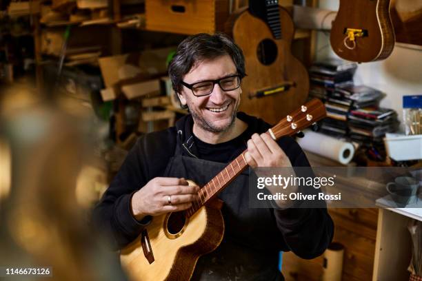 happy instrument maker playing on ukulele in his workshop - melody maker fotografías e imágenes de stock