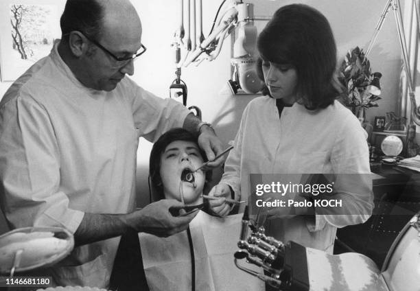 Dentiste soignant un enfant dans son cabinet aidé par son assistante, Suisse.