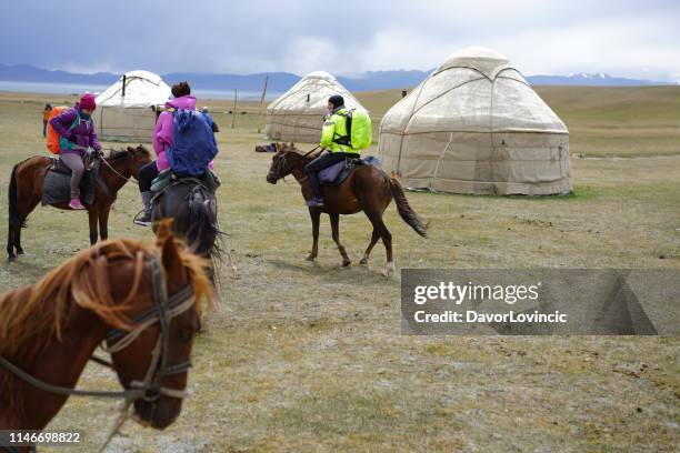 tourists passing yurtas on horseback riding tour, heading to lake song kol, kyrgyzstan - yurt stock pictures, royalty-free photos & images