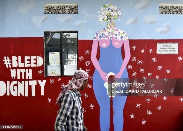 An Indian man looks on as he walks along a wall painting about female menstruation at the school for underprivileged children, Parijat Academy, on...