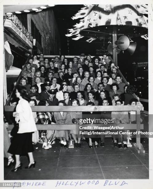 View of film fans as they sit in bleachers erected on the sidewalk of Hollywood Boulevard for a nighttime movie premiere, Los Angeles, California,...