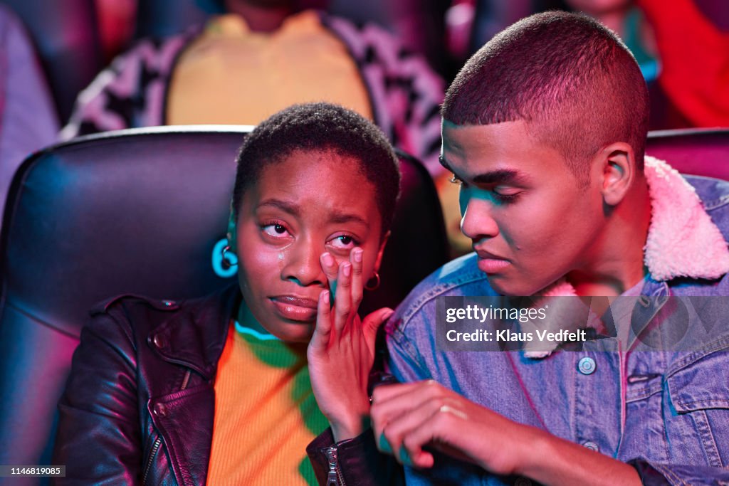 Young man looking at woman crying while watching movie in theater