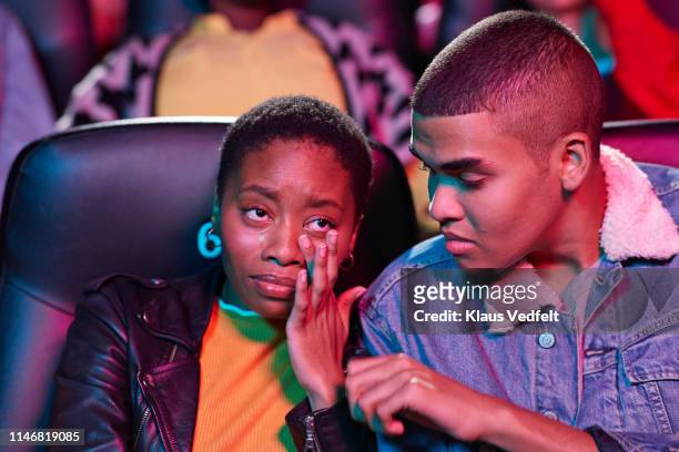 young man looking at woman crying while watching movie in theater - black theatre stock pictures, royalty-free photos & images