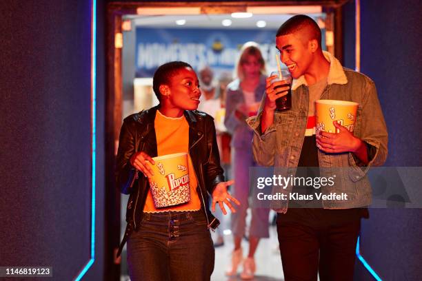 Smiling young friends talking while walking in corridor at movie theater