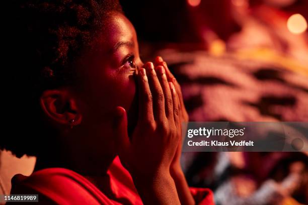 side view of shocked girl covering mouth while watching thriller movie in theater - kind staunen stock-fotos und bilder