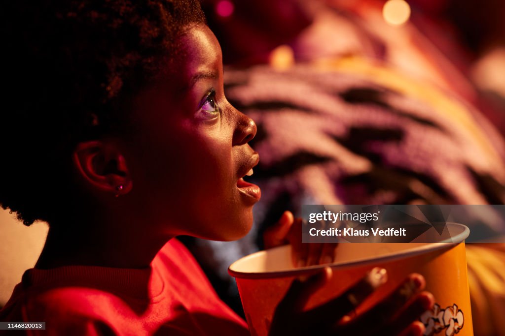 Shocked girl with popcorn watching thriller movie in cinema hall at theater