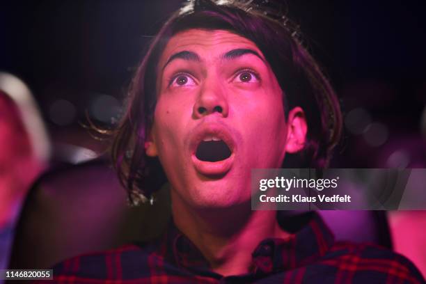 surprised young man with mouth open watching horror movie in cinema hall at theater - ongeloof stockfoto's en -beelden