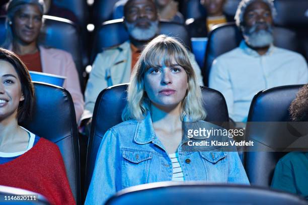 young blond woman watching movie with smiling friend in theater - filmindustrie stock-fotos und bilder