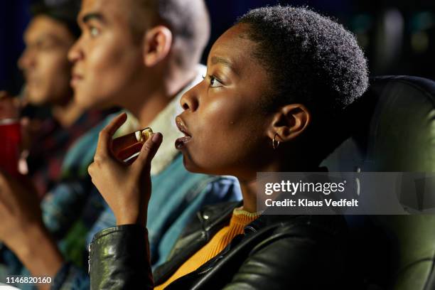 side view of young woman eating snack while watching thriller movie in cinema hall at theater - dramafilm stockfoto's en -beelden