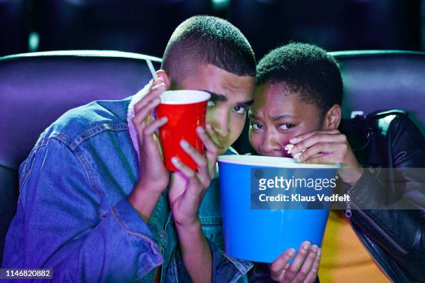 frightened young couple hiding while watching horror movie together at cinema theater - scary movie stockfoto's en -beelden