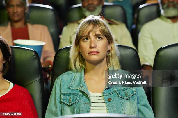 young blond woman with blank expression watching movie in theater - filmdrama stock-fotos und bilder