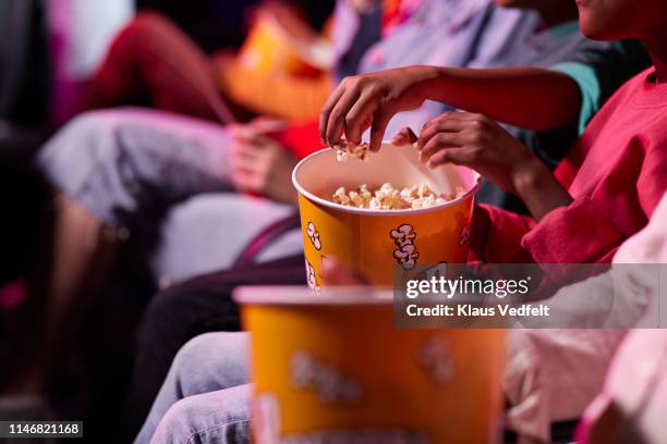 midsection of friends sharing popcorn while sitting in theater - 映画館 ストックフォトと画像