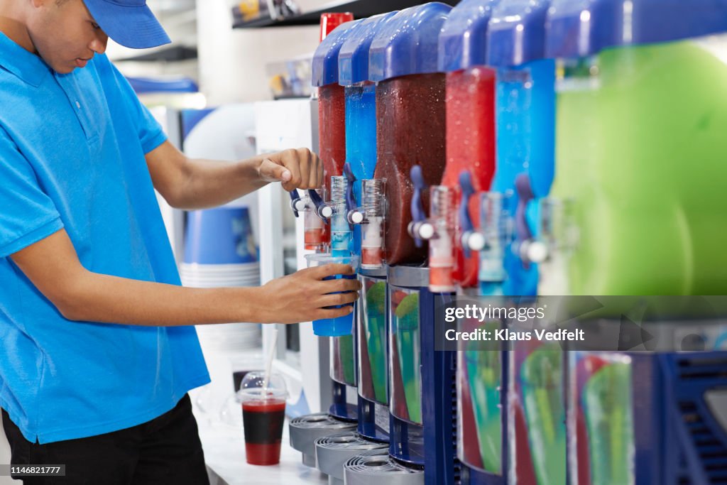 Male employee filling soda in cup from machinery