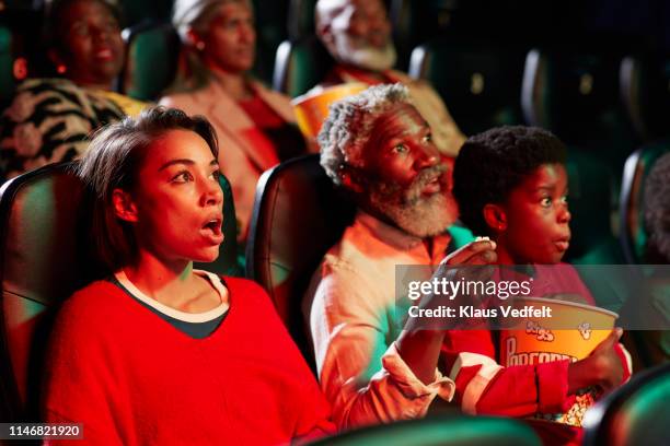 surprised young woman watching horror movie by spectators in theater - woman watching horror movie stock pictures, royalty-free photos & images