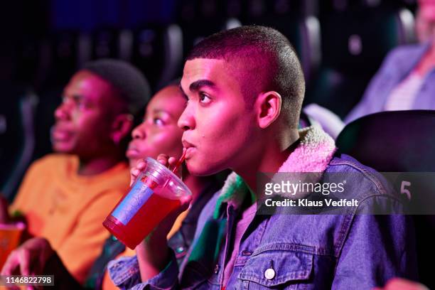 Close-up of young man drinking soda while watching movie in cinema hall
