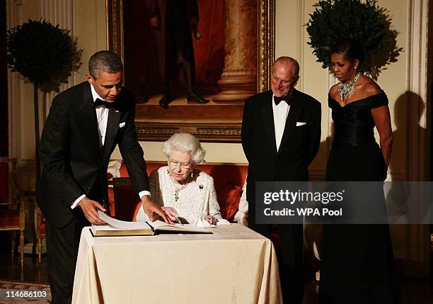 Queen Elizabeth II signs the guest book as she bids farewell to U.S. President Barack Obama and First Lady Michelle Obama, watched by the Duke of...