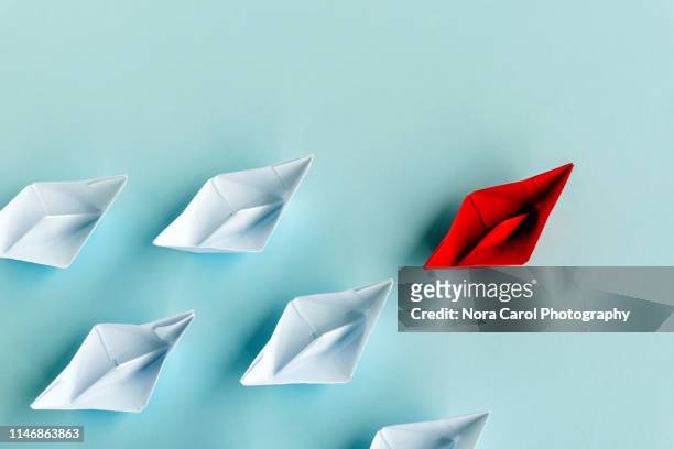 leadership concept - red paper boat followed by white paper boat on blue background - seguir actividad móvil general fotografías e imágenes de stock