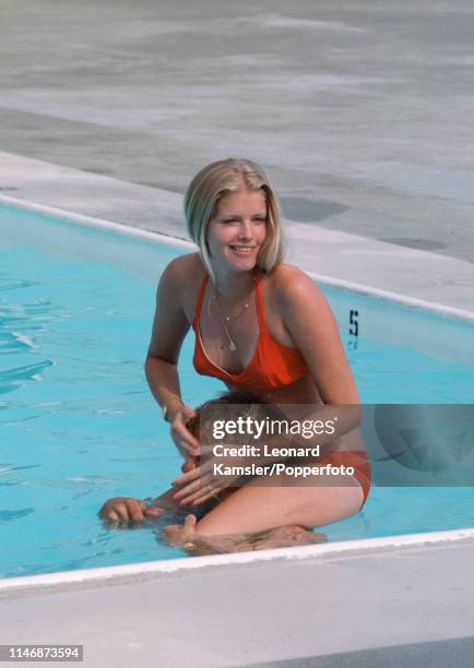 Polly Crenshaw, wife of American golfer Ben Crenshaw, sits atop his shoulders in a swimming pool, circa 1976.